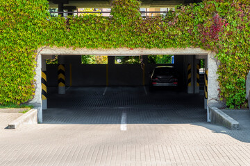 Multi-storey garage entrance. Facade is overgrown by creepers