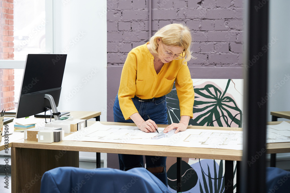 Poster female construction engineer working at office desk, she drawing on a building project with a pencil
