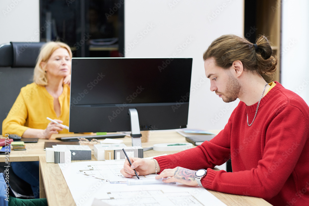 Poster Young professional designer drawing design building project in office with his colleague working on computer in background