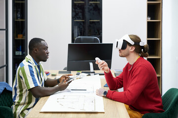 Business colleagues sitting at table opposite each othe and using virtual reality goggles at their work at office