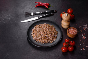 Delicious fresh boiled buckwheat porridge with vegetables and spices on a black plate