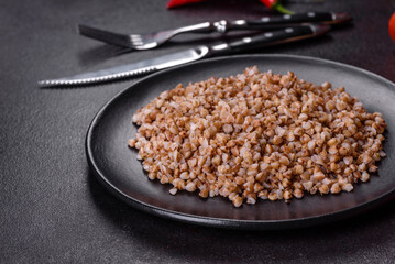 Delicious fresh boiled buckwheat porridge with vegetables and spices on a black plate