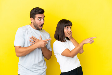 Young couple isolated on yellow background pointing finger to the side with a surprised face