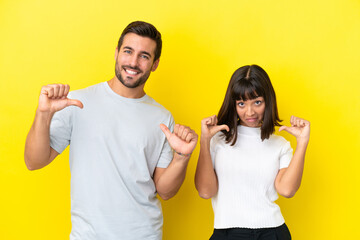 Young couple isolated on yellow background proud and self-satisfied in love yourself concept