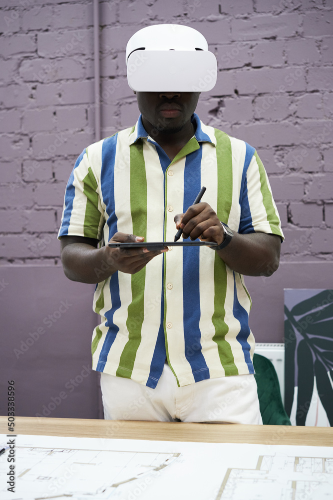 Poster Portrait of African graphic designer using virtual reality goggles to use graphic tablet while standing at office
