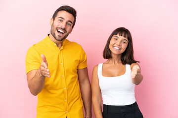 Young couple isolated on pink background shaking hands for closing a good deal