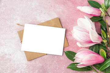 Blank greeting card with pink magnolia flowers and green leaves on pink concrete background. Flat lay. Mock up