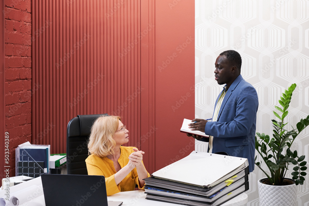 Poster african businessman talking to manager and making notes in notebook during their conversation at off
