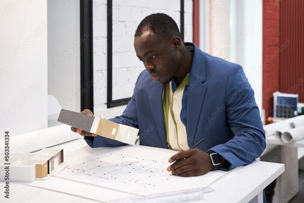Poster serious african architect looking at samples and drawing plan of new building at table
