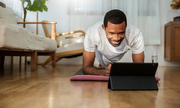 Portrait of young African American black man warm up exercise workout yoga plank position at home living room. Yoga for beginner. Guy watching online tutorials on tablet, training, healthy stay home