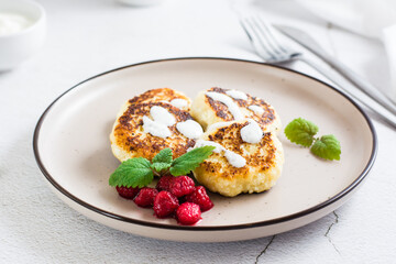 Cottage cheese pancakes with sour cream, raspberries and mint on a plate on the table.