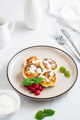 Cottage cheese pancakes with sour cream, raspberries and mint on a plate. Vertical view. Close-up