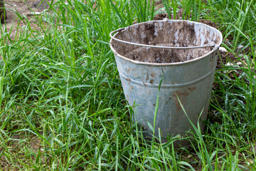 Old dirty bucket stained with paint on the street on the grass. Used metal bucket.