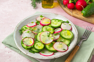 Radish salad with cucumber, dill, onion and olive oil in a plate with fork on pink concrete background. close up