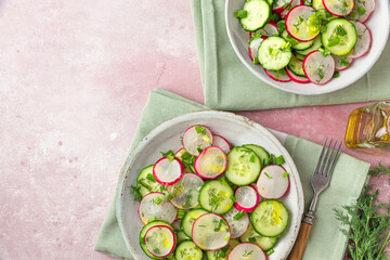Summer radish salad with cucumber, dill, onion and olive oil in a plate with fork on pink concrete background. Top view