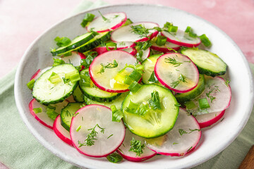 Fresh summer salad with radish, cucumbers, onion, dill and olive oil in a bowl on pink background. close up