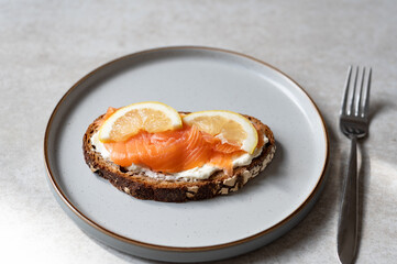 Toasted bread with cheese cream, salmon and lemon slices on grey plate