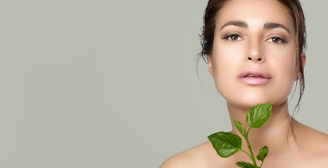 Natural beauty with green leaves near face. Beautiful woman with fresh hydrated and glowing skin....