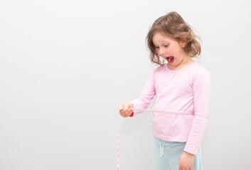 Caucasian girl 6 years old, in a yellow sweatshirt with a hood on a gray background. The child poses for the camera, measures his waist and is surprised.