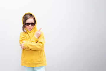 Caucasian girl 6 years old, in a yellow sweatshirt with a hood on a gray background. The child smiles and poses for the camera, showing a 