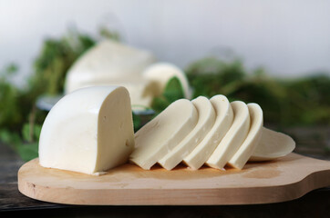 Sliced cheese on a wooden board with green herbs background. Georgian cheese sulguni, selective focus