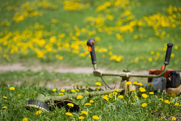 Close-up of a lawn mower lying on the grass. A worker mows the grass on the side of the road or in...