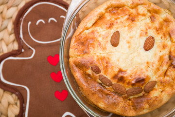 Freshly baked apple pie with almond nuts in the form of a smile in a glass dish on a wicker background with a stick in the form of a gingerbread.