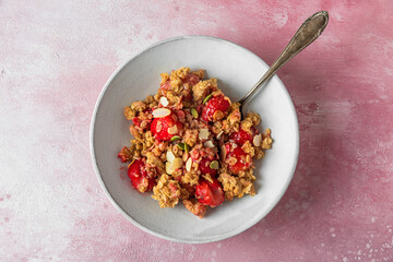 Berry crumble pie with strawberry, oat flakes, almonds and pumpkin seeds in a plate with spoon on pink background