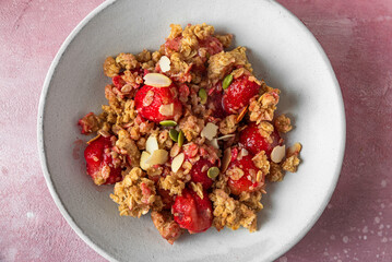 Delicious strawberry crumble with oats, almonds and pumpkin seeds in a plate on pink background. Close up