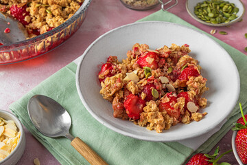 Delicious strawberry crumble with oats, almonds and pumpkin seeds in a plate on pink background. Close up