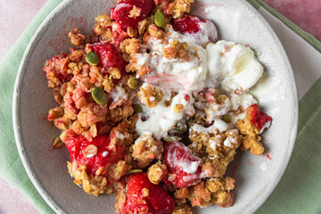 Delicious strawberry crumble with ice cream, oats, almonds and pumpkin seeds in a plate on pink background