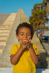 Fototapeta na wymiar Black boy eating a cookie with chocolate. Dressed in yellow t-shirt, African American boy