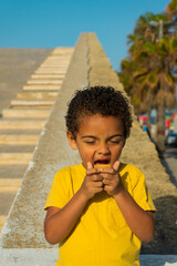 Fototapeta premium Black boy eating a cookie with chocolate. Dressed in yellow t-shirt, African American boy