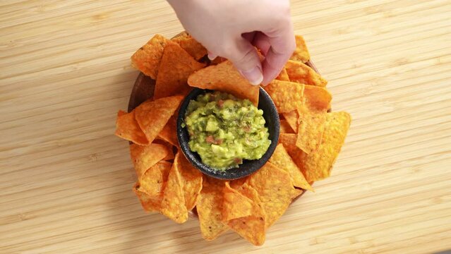 4k video, Eating Traditional Mexican food. A hand taking cooked nachos served with meat and vegetables, tomato soup with cilantro, guacamole top view from wooden tray. Eating cheese Potato Chips
