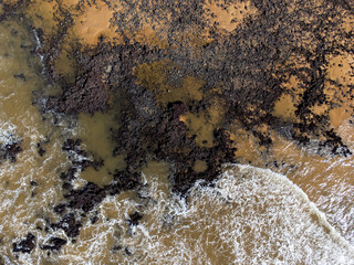 Beautiful beach with dark sands and black rocks like a volcano. Manguinhos, Espirito Santo, Brazil - aerial drone view