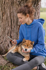 a woman with a dog in the park does sports or fitness on a yoga mat. a European woman with curly hair in a blue hoodie is chatting on a smartphone and playing with a dog. a happy woman is resting