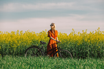  girl in vintage dress and sunglasses with bicycle in rapeseed field