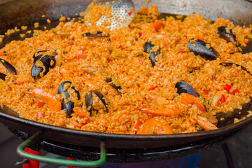 Orange paella with shrimp, mussel, rice, spice, saffron in huge paella pan at summer outdoor food market: close up. Spanish cuisine, seafood, gastronomy, street food concept