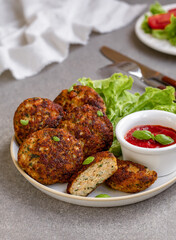 Juicy homemade meatballs (meat cutlets) served on a plate with green salad and tomato dipping sauce. Selective focus, gray concrete background. Vertical.