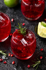 Pomegranate gin cocktail with lime, rosemary and ice on rustic black table