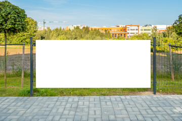 Blank white banner for advertisement on the fence. Residential area with modern buildings and tower crane in the background.