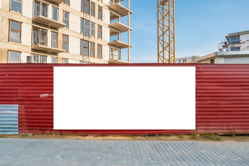 Blank white advertising banner on the fence of construction site. Residential area with modern...