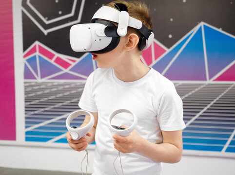 Boy using VR glasses exploring augmented reality, using smart devices, controllers in hands. Modern cyber technologies concept, Virtual reality games on colourful background. Very peri 2022. Play room