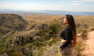 Naklejka premium Portrait of Latin woman dressed in black with a cap having fun during the day of trekking in the mountain forest - looking at the horizon