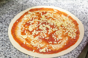 The process of preparing pizza. The chef pours tomato sauce over the rolled dough.