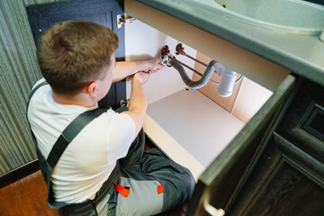 A male plumber repairs siphon under the sink in the bathroom.