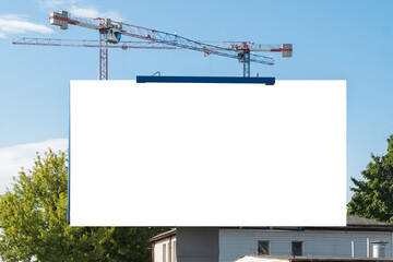 Blank white billboard for advertisement near construction site with tower cranes