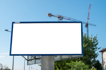 Blank white billboard for advertisement near construction site with tower cranes