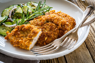 Breaded fried pork chop with sliced cucumbers and rosemary on wooden table
