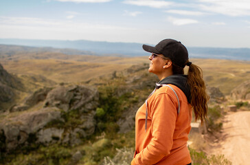 Portrait of latin woman dressed in orange with a cap and tail turned back having fun during the day of trekking in the mountain forest - looking at the horizon